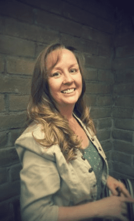 A woman smiling for the camera in front of a brick wall.